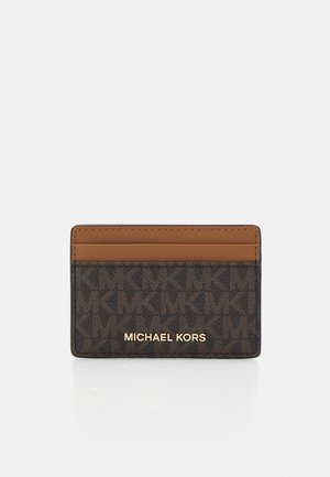 Michael Kors'i kaarditasku pruunis, millel on reljeefne logo muster, lisatud heledat pruunikat triipu ja kuldne logo tekst. Kompaktne ristkülikuline kuju.