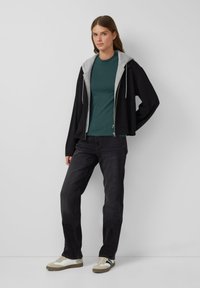 Czarna bluza z zamkiem błyskawicznym z szarym wnętrzem, turkusowa koszula, ciemne dżinsy i beżowe buty sportowe z czarnymi akcentami. Prosty, codzienny design.