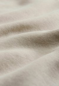 Tela de color beige claro que muestra una fina textura con un tejido visible y un suave caído, resaltando su superficie lisa y su maleabilidad.