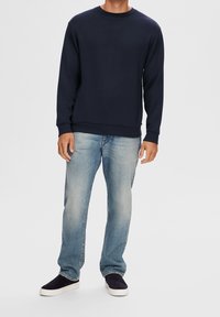 Navyblå sweatshirt med långa ärmar och rund halsringning, ihop med ljusblå jeans och mörka mockasiner.