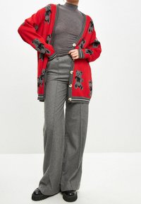 Cardigan rosso con motivi di orso grigi, dettagli a coste e grandi bottoni, indossato sopra un dolcevita grigio e pantaloni grigi a gamba larga. Scarpe platform nere.