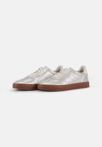 Silver leather sneakers with a textured finish, featuring a tan rubber sole and white laces, designed with a low-top silhouette.