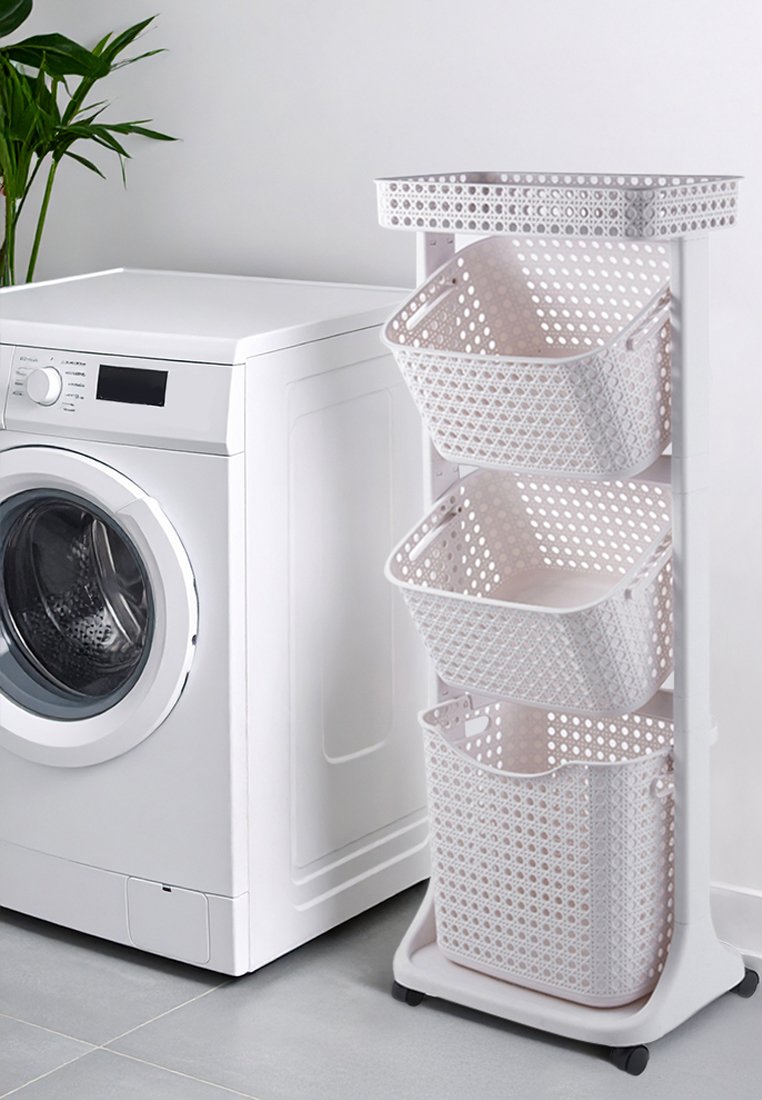 Trójwarstwowy sorter do prania z białymi perforowanymi koszami, umieszczony na smukłej białej ramie na kółkach, ustawiony obok pralki.
