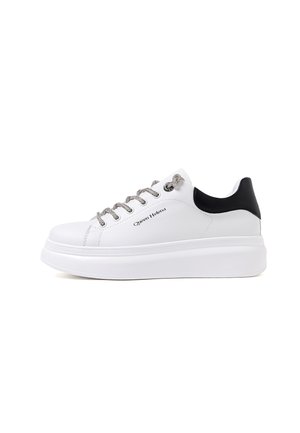 Sneaker bianco con suola a piattaforma spessa, dotato di accenti neri sul tallone e lacci argentati. Parte superiore realizzata in materiale sintetico liscio.