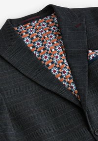 Blazer cu model închis, având un exterior texturat și o căptușeală vibrantă cu model geometric în nuanțe de portocaliu, albastru și crem. Include un batic.