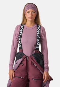 Paarse longsleeve-top onder een zwarte en maroon skibroek met verstelbare banden. Opvallende ritszakken en een textuur hoofdband met patroon.