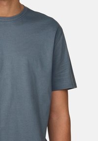 T-Shirt mit kurzen Ärmeln in Teal, aus weichem Baumwollmaterial, mit rundem Hals und normaler Passform. Nahtdetails an den Ärmeln sichtbar.