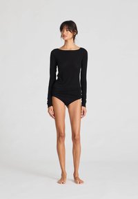 Svart långärmad topp med bred halsringning, figursydd kropp och slät yta, kombinerad med svarta högskurna trosor. Minimalistisk design.