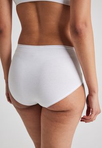 Braguitas blancas de algodón de cintura alta con una textura suave y una cintura elástica, que presentan costuras mínimas y sin detalles de hardware visibles.