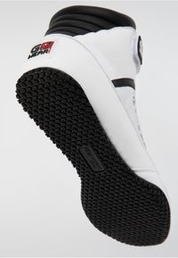 Witte hoge sneaker met een zwarte rubberen zool, gestructureerd oppervlak en grijze accenten. GEAR-logo zichtbaar op de hiel en zijkant.