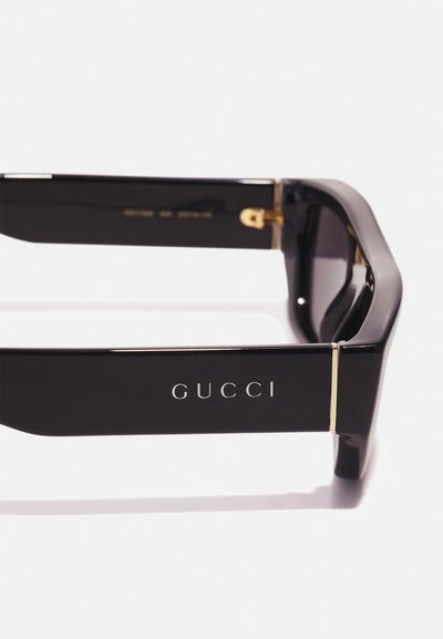 Črne Gucci sončna očala z drzno, angularno obliko. Imajo zlate akcentne detajle in vgraviran logotip na ročaju. Sijajna površina, temna leča.