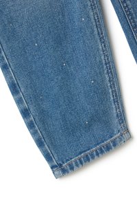 Jeans de mezclilla en azul medio con ligero desgaste, con detalles de tachuelas plateadas esparcidos por la tela. Dobladillo limpio y costura estándar.