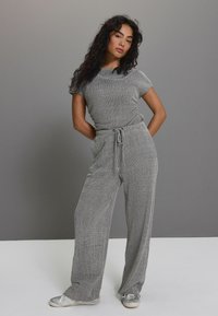 Šedý pletený dvoudílný outfit, skládající se z trička s krátkým rukávem a kalhot s širokými nohavicemi a stahovacími pasem; měkká textura a volný střih.