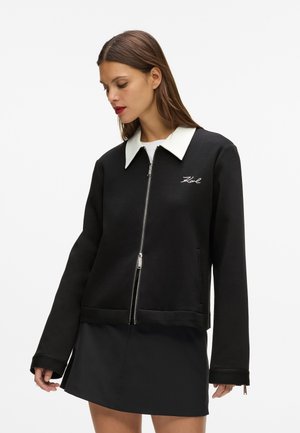 Black zip-up sweatshirt with a white collar, featuring a front pocket and ribbed cuffs. Simple design with embroidered logo on the chest.