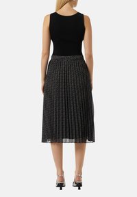 Czarna prążkowana dopasowana bluzka z plisowaną spódnicą midi, na której znajduje się subtelny biały wzór spiralny. Modelka nosi sandały na srebrnych obcasach.