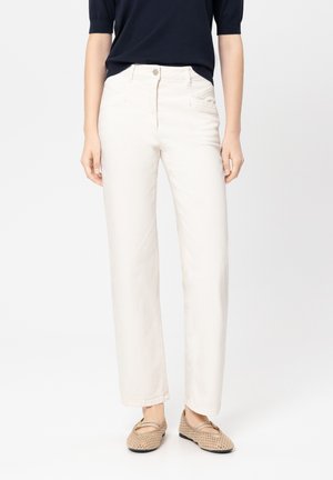 Light beige straight-leg jeans with front pockets, a metal button closure, and subtle stitching details. Worn with a navy top and woven shoes.