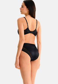 Ensemble de lingerie noire composé d'un matériau extensible sans coutures avec des accents en dentelle sur les côtés. Bretelles réglables et fermeture à agrafe dans le dos.