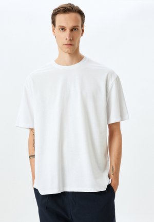 Vit bomull t-shirt med avslappnad passform, rund hals, korta ärmar, utan mönster, visad mot en ljus bakgrund.