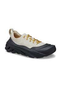 Scarpa sportiva beige chiaro con lacci gialli, tomaia in tessuto a texture, suola in gomma scura e un design ondulato distintivo. Punta e tallone rinforzati.