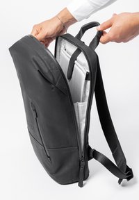 Zaino in pelle nera dal design elegante, con tasca frontale con zip e scomparto interno per laptop foderato con tessuto a motivi a griglia.