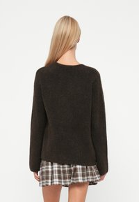 Dunkelbrauner, flauschiger Pullover mit langen Ärmeln, Rundhalsausschnitt und einem leicht oversized Schnitt, kombiniert mit einem karomusternden Lagenskirt.
