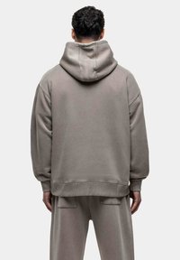 Lichtgrijze oversized hoodie met een grote kap, ribgebreide manchetten en zoom, gemaakt van zacht materiaal, met een relaxte pasvorm en minimale stikdetails.