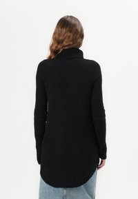 Pull noir en maille avec un col montant et une texture côtelée. Présente un ourlet arrière plus long, associé à un jean en denim bleu clair.