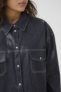 Tume denimpaita läikiva viimistlusega, terava krae, kahe esipocketiga ja valge õmblusega. Omab nupuvajutusega kinnitusi.