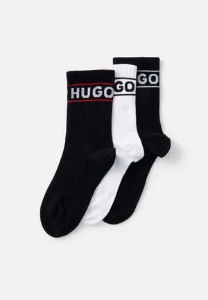 Trois paires de chaussettes de sport : une paire noire avec des rayures rouges, une paire noire avec des rayures blanches et une paire blanche avec des rayures noires. Texture côtelée.