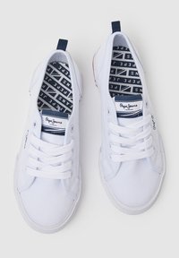 Scarpe da ginnastica bianche in tela con suola piatta, design con lacci e soletta a fantasia blu navy. Presentano una piccola linguetta blu e dettagli rossi.