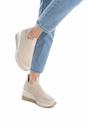 Piernas vestidas con jeans azul claro y zapatillas de cuña de punto beige, todo contra un fondo blanco.