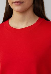 Rode katoenen T-shirt met ronde hals, voorzien van een soepele textuur en minimale stikdetails rond de halslijn.