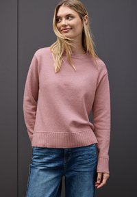 Helles rosa Sweatshirt mit geripptem Saum und Bündchen, aus einem weichen Stoff gefertigt, kombiniert mit blauen Jeans. Einfaches, lässiges Design.