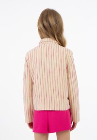 Světle béžová a růžově pruhovaná bunda s dlouhými rukávy, límečkem a rovnými střihy, doplněná jasně růžovými šortkami. Texturovaná látka.