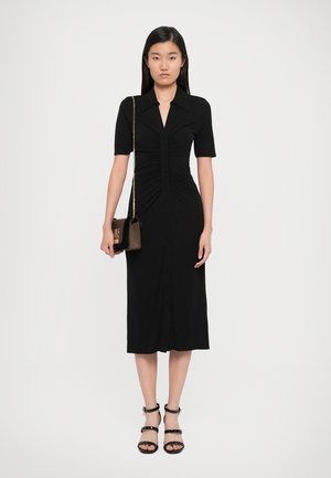 Black button-up dress with short sleeves, ruched bodice, and a mid-calf length. Paired with black strappy heels and a small bag.