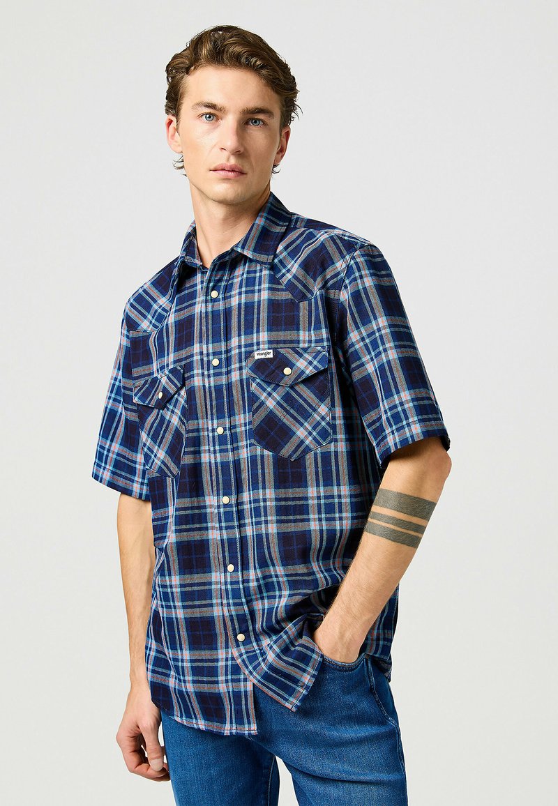 Camicia a maniche corte a quadri in blu navy e blu, con due tasche sul petto, chiusure con bottoni e una patch in tessuto con logo sulla tasca sinistra.