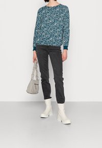 Teal mönstrad tröja med långa ärmar, matchad med svarta tajta jeans. Vita ankelstövlar och en ljusgrå handväska med en texturerad rem.