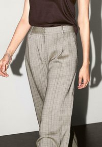 Pantaloni a quadretti grigio chiaro con una vestibilità ampia, dotati di tasche laterali e un design frontale piatto. Il tessuto ha una texture liscia con un leggero lucido.