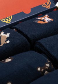 Marineblaue Socken mit einem Strickmuster von verspielten Füchsen in Orange und Braun, verpackt in einer bunten Box mit geometrischem Design.