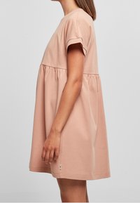 Helles rosa Baumwollkleid mit kurzen Ärmeln, rundem Ausschnitt und geraffter Taille, mit einer lockeren, fließenden Silhouette und seitlichem Logo-Acccent.