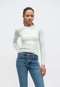 Ανοιχτό γκρι μακρυμάνικη μπλούζα σε εφαρμοστή γραμμή, κατασκευασμένη από απαλή υφή, σε συνδυασμό με τζιν παντελόνι ψηλόμεσο σε μπλε χρώμα. Απλό, χωρίς σχέδια.