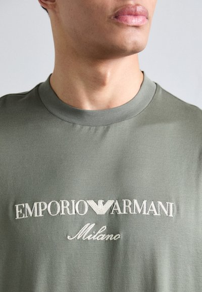 Oliivroheline t-särk klassikalise ümara kaelusega, millel on kerge beeži värvi tikand "EMPORIO ARMANI Milano" logo ja sile kangastekstuuri.