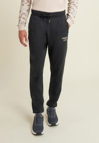 Pantaloni della tuta neri con vita elasticizzata e cordino, dotati di tasche laterali e logo stampato. Tessuto leggero con texture liscia.