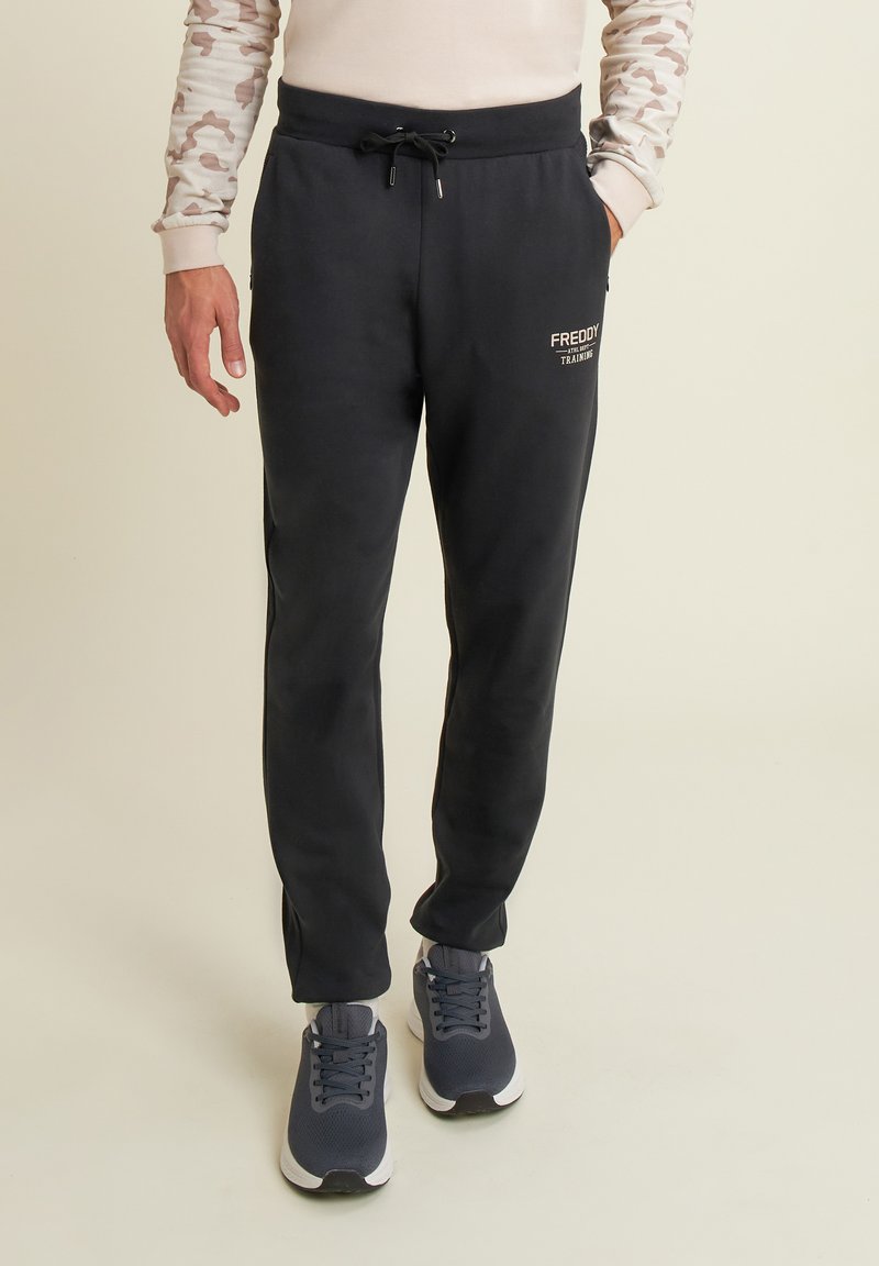Pantaloni della tuta neri con vita elasticizzata e cordino, dotati di tasche laterali e logo stampato. Tessuto leggero con texture liscia.