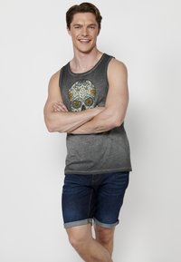 Sötét szürke ujjatlan felső, színes koponya mintával és virágos díszítéssel, kék denim rövidnadrággal párosítva. Simább anyagtextúra.