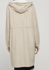 Chaqueta con capucha beige, con cintura elástica, mangas largas y textura suave. Presenta un diseño sencillo y llega a la mitad del muslo.