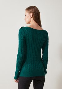 Dark green knit sweater with a cable texture, wide neckline, and ribbed cuffs and hem. Features long sleeves and a form-fitting silhouette.
