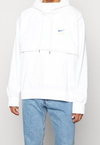 Valkoinen huppari, jossa on korkea kaula-aukko, säädettävät nyörit ja etutasku. Sisältää sinisen ja keltaisen Nike AIR -logon. Pehmeä kangasrunko.