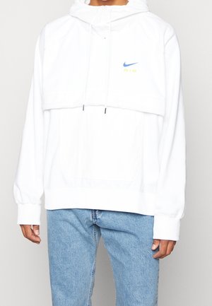 Sudadera blanca con cuello alto, cordones ajustables y un bolsillo frontal. Presenta el logo de Nike AIR en azul y amarillo. Textura de tela suave.