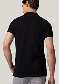 Czarna koszulka polo z krótkim rękawem, standardowym kołnierzykiem i dyskretnym logo na plecach. Wykonana z gładkiego, lekkiego materiału.